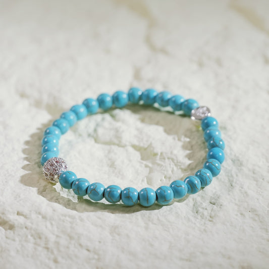 A handmade stretch bracelet with turquoise beads, a gold CZ accent, and Gina Kim logo charm. Peaceful and refreshing.
