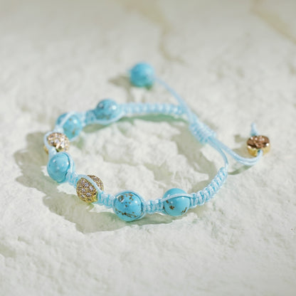 A handmade turquoise macramé bracelet featuring natural turquoise beads and gold-plated CZ accents, finished with an adjustable sliding knot and Gina Kim branding. Displayed in a luxury satin-lined gift box