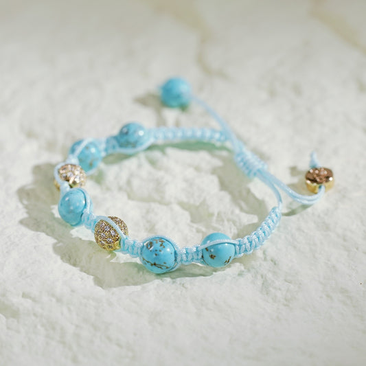 A handmade turquoise macramé bracelet featuring natural turquoise beads and gold-plated CZ accents, finished with an adjustable sliding knot and Gina Kim branding. Displayed in a luxury satin-lined gift box